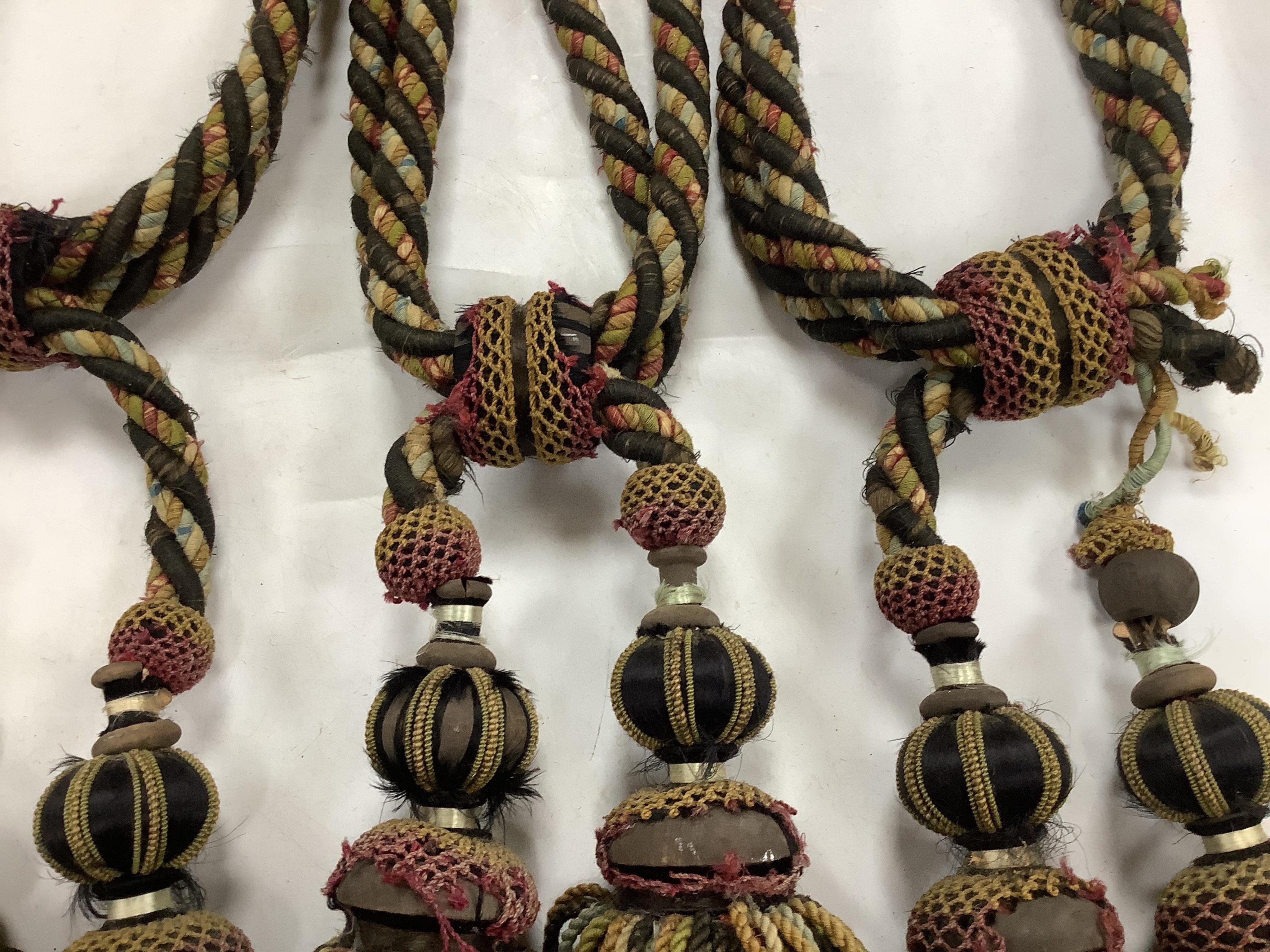 Four pairs of late 19th early 20th century corded and tasseled black and multicoloured tie backs. 69 cm long. Condition - all worn from use and age, one tassel needs repair.
